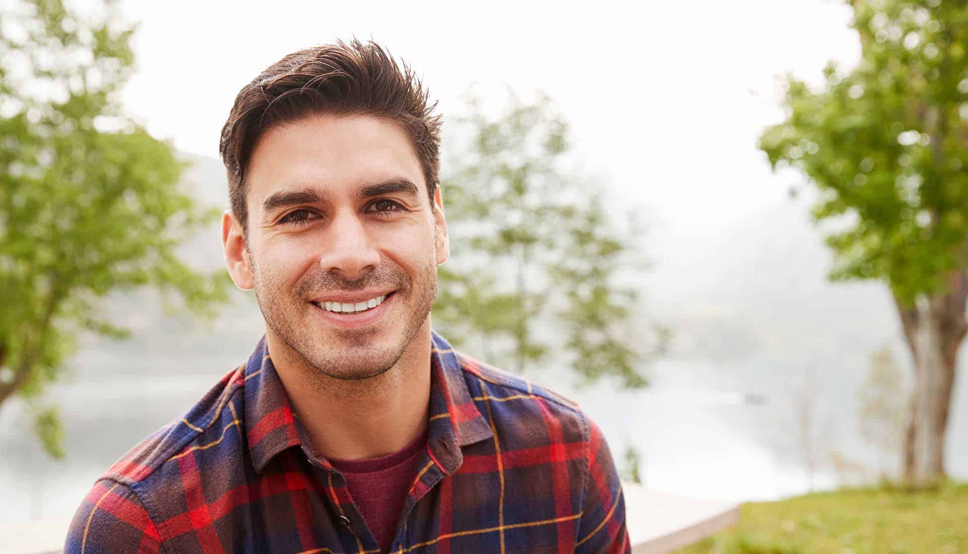 Young Hispanic man in a park smiling.