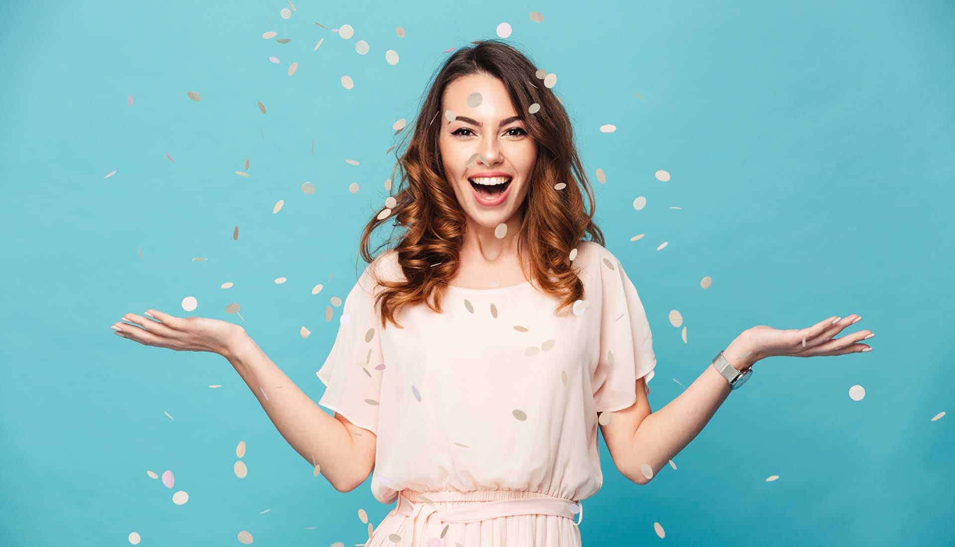 Portrait of a cheerful beautiful girl wearing dress standing standing under confetti rain.