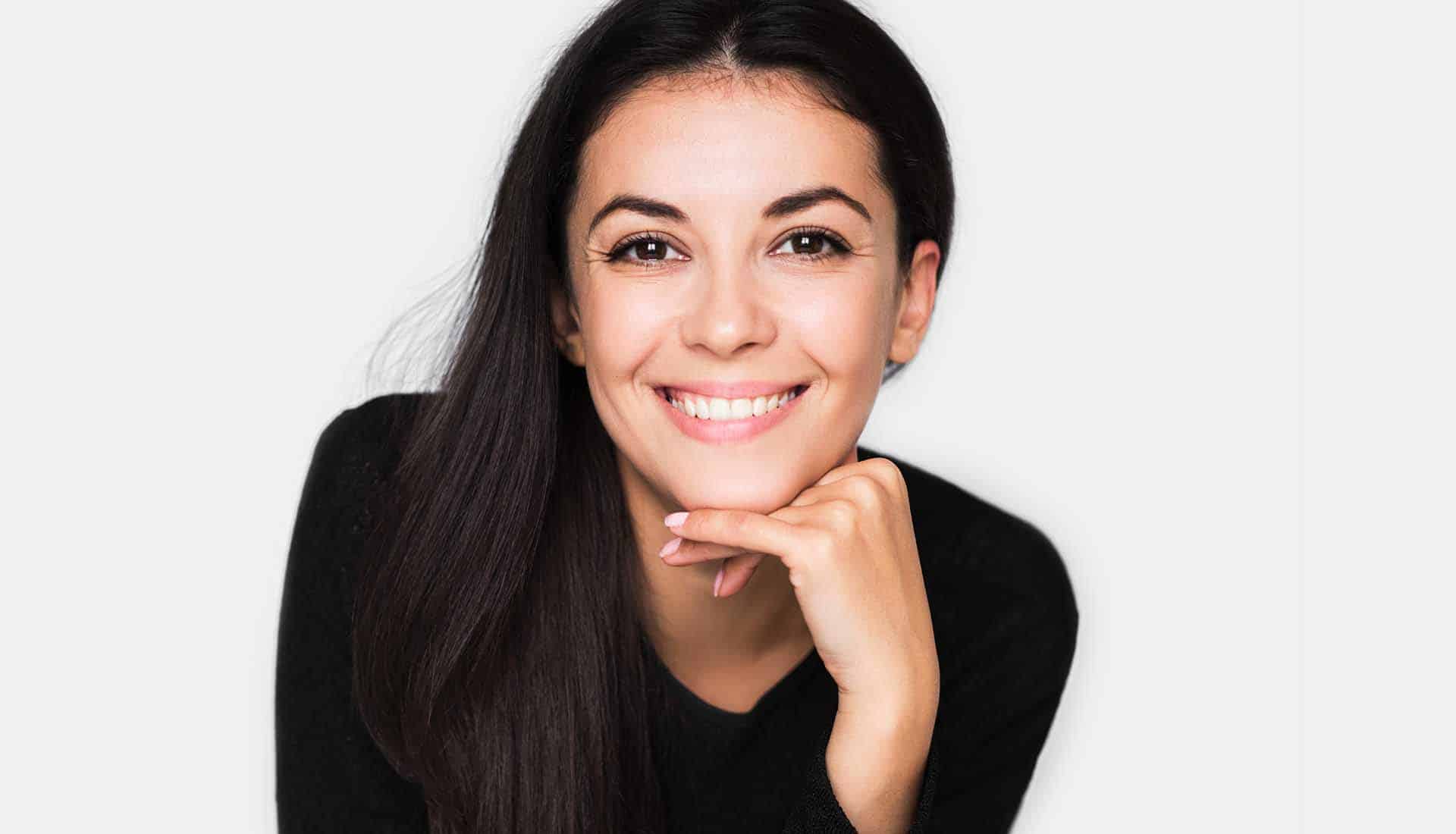 Portrait of brunette cute woman with beautiful and healthy toothy smile, with hand on chin.