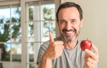 Smiling mature man eating an apple and showing his thumb up.
